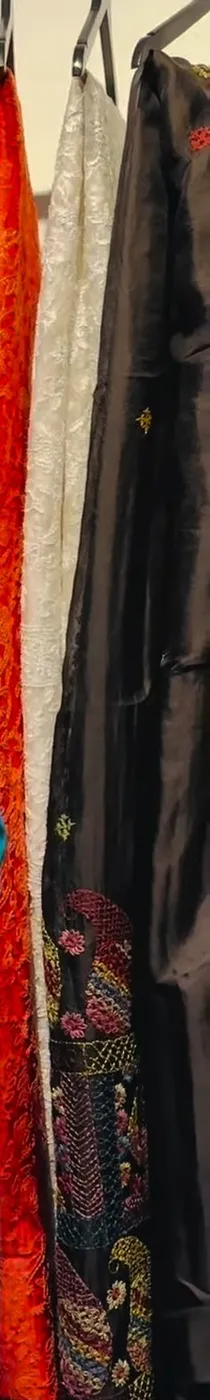 A black saree with a printed border beside a red one